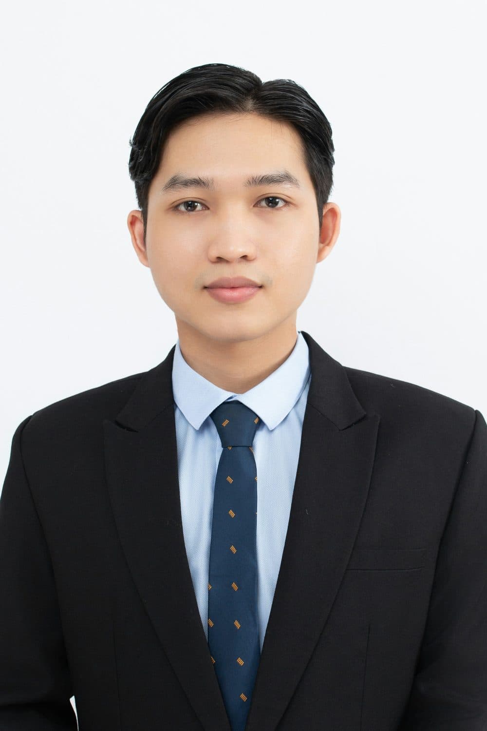 A man in a black suit and blue tie facing the camera against a plain white background