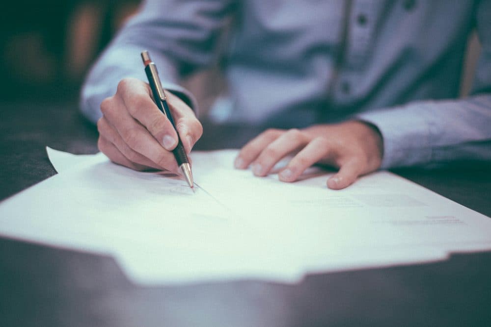 A hand signing a sheet of paper with a pen at a desk
