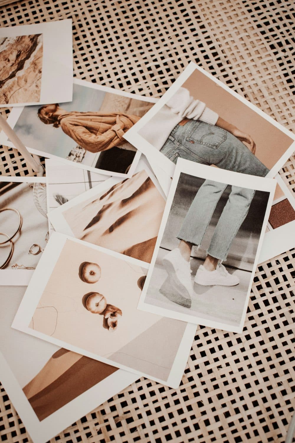 A scattered pile of printed photographs of clothing and still-life scenes lying on a woven rattan surface