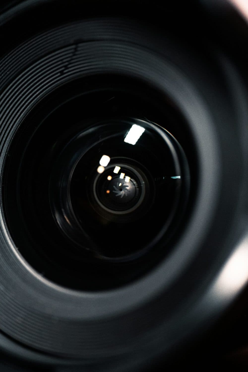 A close up of a camera lens with the aperture blades and bright window reflections visible deep inside the dark glass