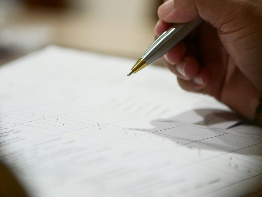 A hand holding a ballpoint pen over a printed paper form
