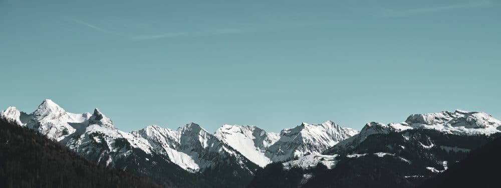 A wide panorama of snow-covered mountain peaks under a clear blue sky
