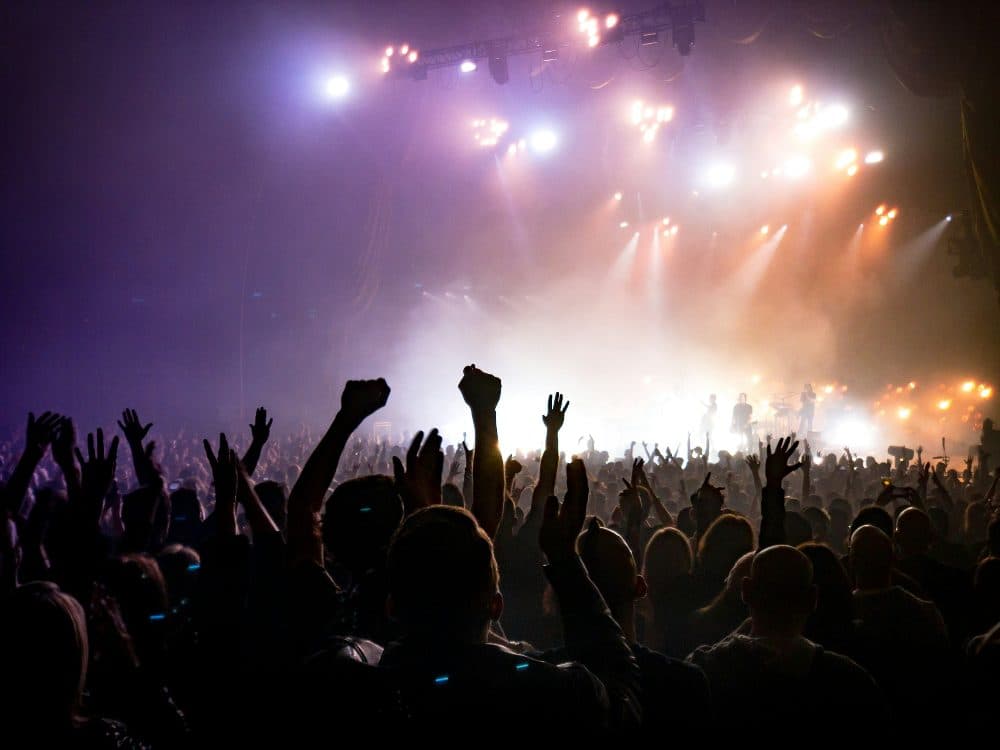 A concert crowd with raised hands facing a brightly lit stage