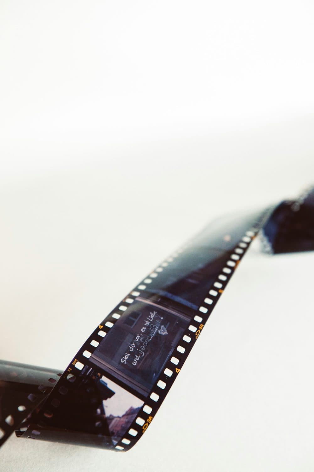 A strip of 35mm film with sprocket holes curling across a bright white surface