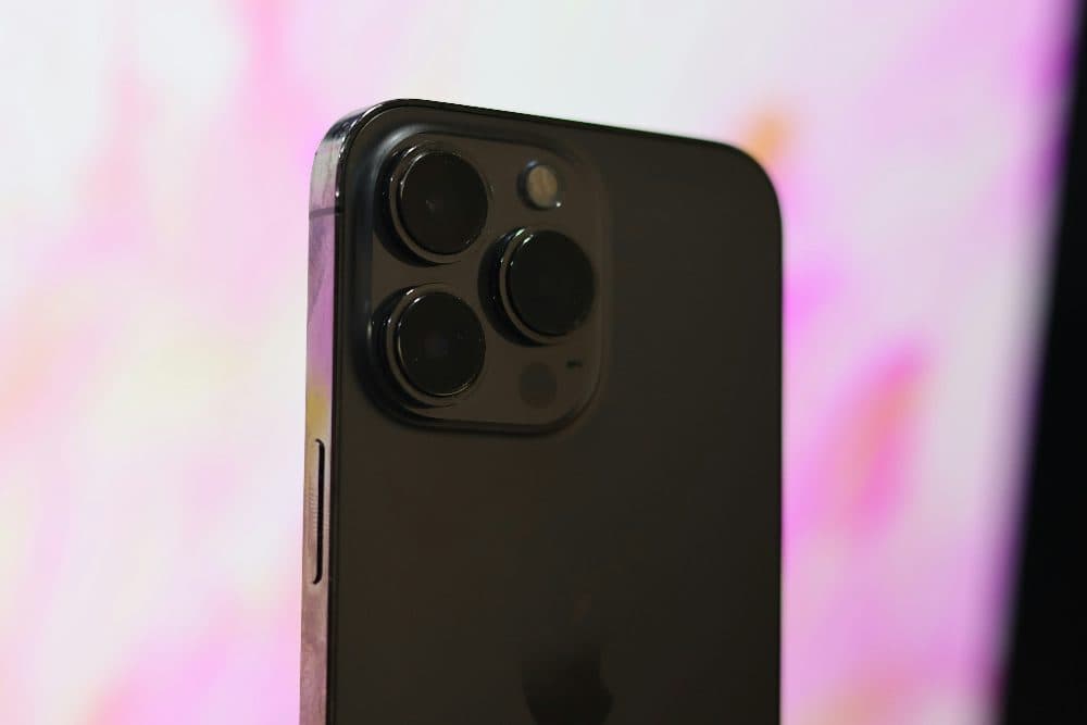 Close-up of the triple camera on the back of a dark smartphone against a soft pink background