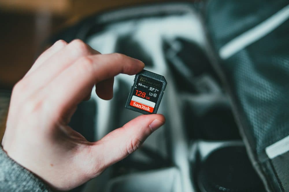 A hand holding a small red and black memory card above an open dark bag