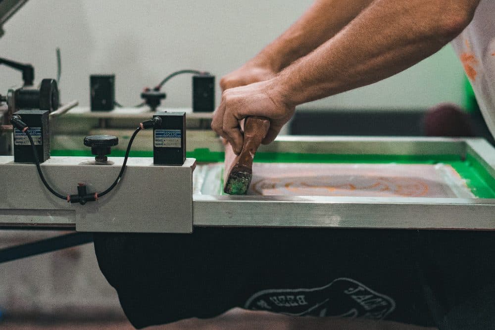 Hands pulling a squeegee across a screen printing press