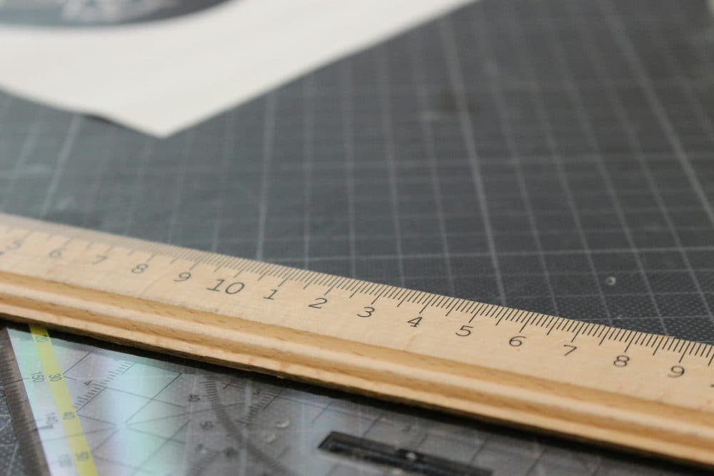 A wooden ruler lying across a grey cutting mat with a printed grid