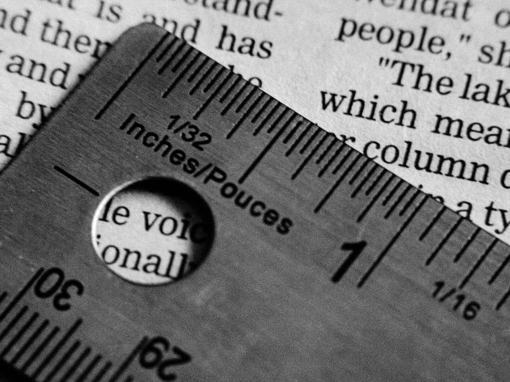 A steel ruler with fine measurement markings and a round hole lying across a printed page of text, in black and white
