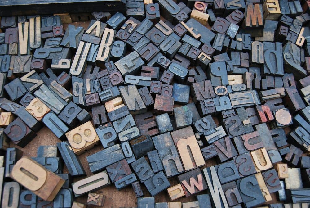 A close-up of a jumbled heap of old wooden letterpress type blocks in assorted sizes and letters lying on a wooden surface