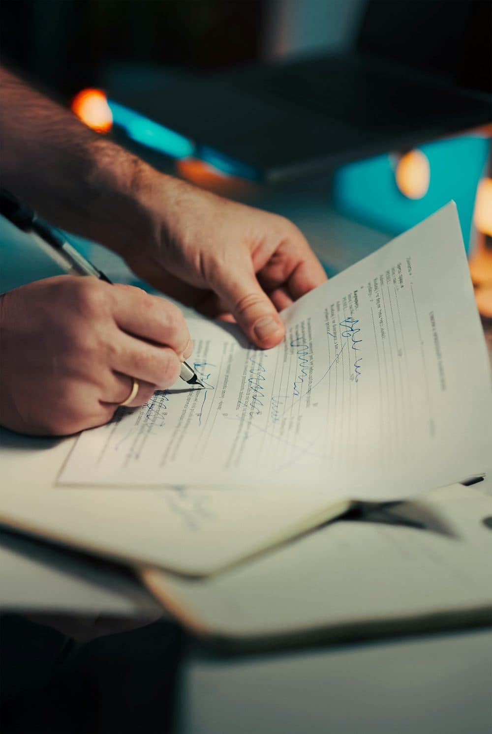 A close-up of a man’s hand holding a pen and signing a printed contract while his other hand steadies the page