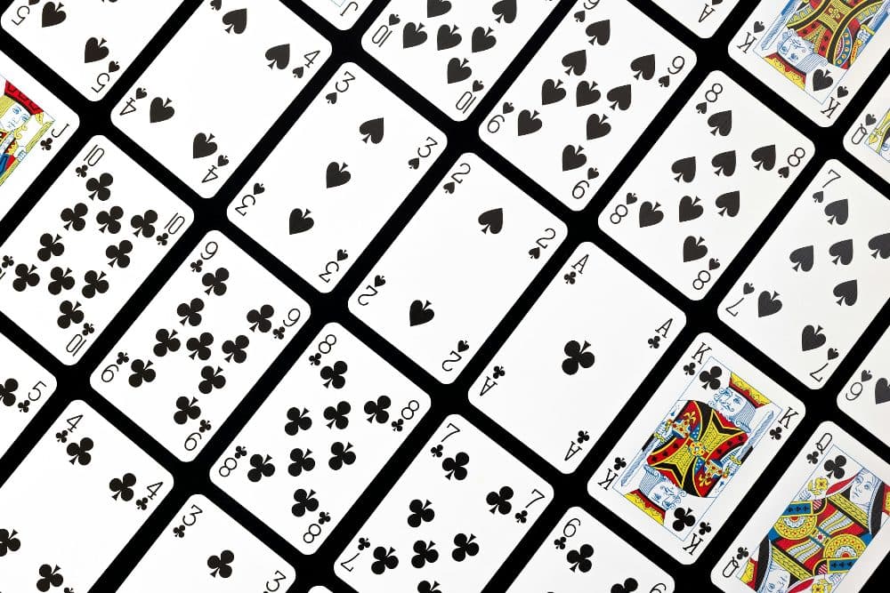 Rows of playing cards laid out in a diagonal grid on a black surface, showing spades and clubs with rounded corners