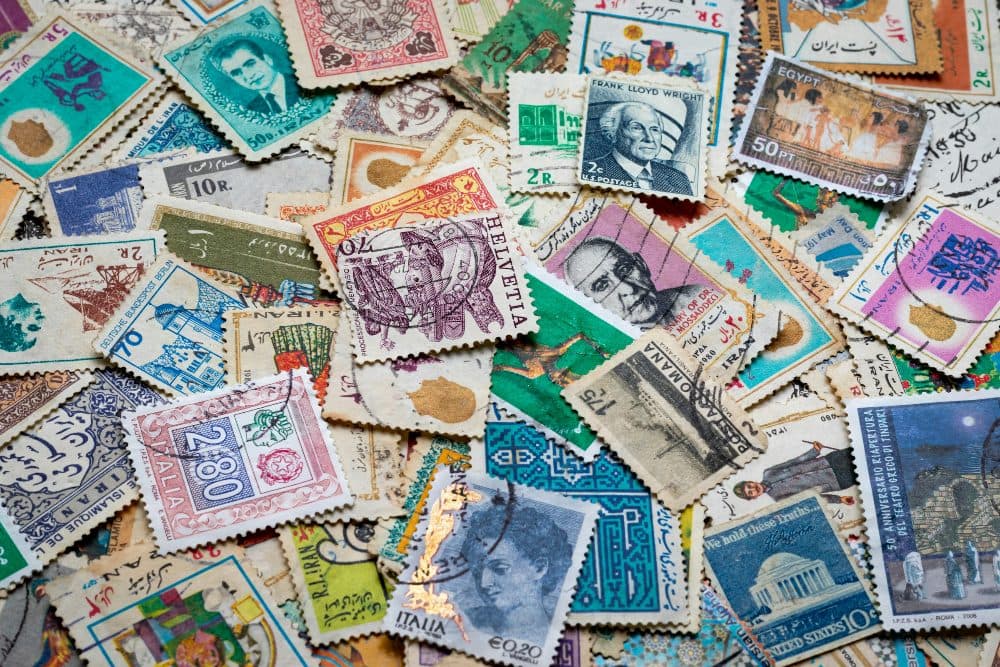 A heap of old postage stamps from many countries spread across a blue and white cloth