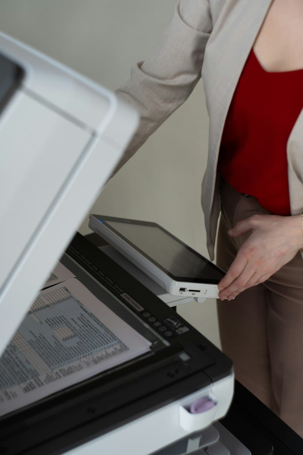 A person in a beige blazer standing beside an office scanner with its lid raised and a printed page lying on the glass