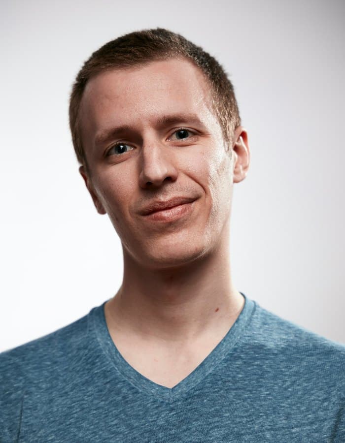 A young man in a blue T-shirt photographed head and shoulders against a plain light grey background