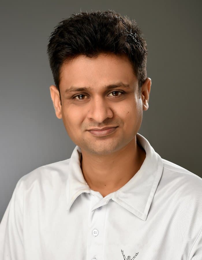 A man with short dark hair in a white polo shirt, photographed head and shoulders against a plain grey background