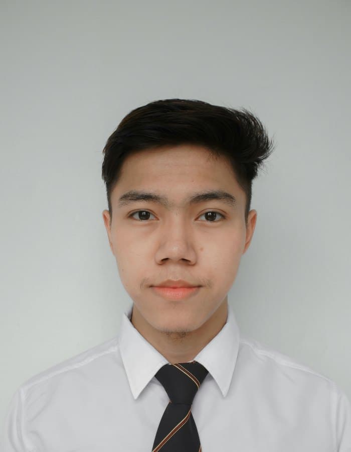 A young man in a white shirt and striped tie, head and shoulders, against a plain pale background