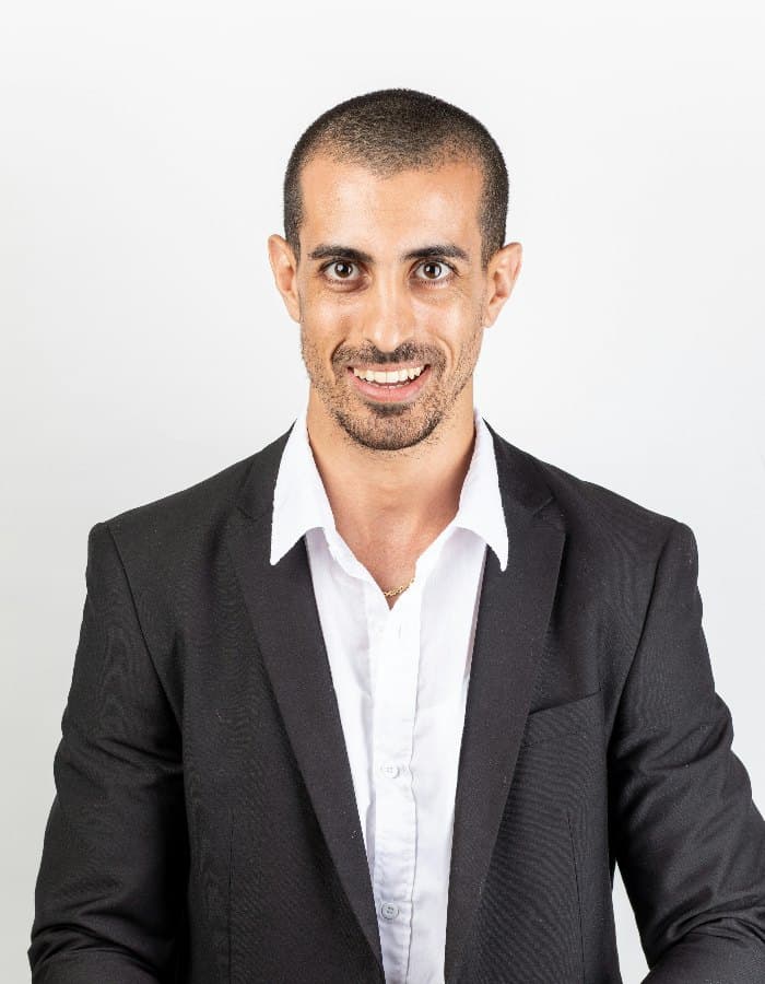 A smiling man in a dark suit jacket and white shirt, head and shoulders, against a plain white background