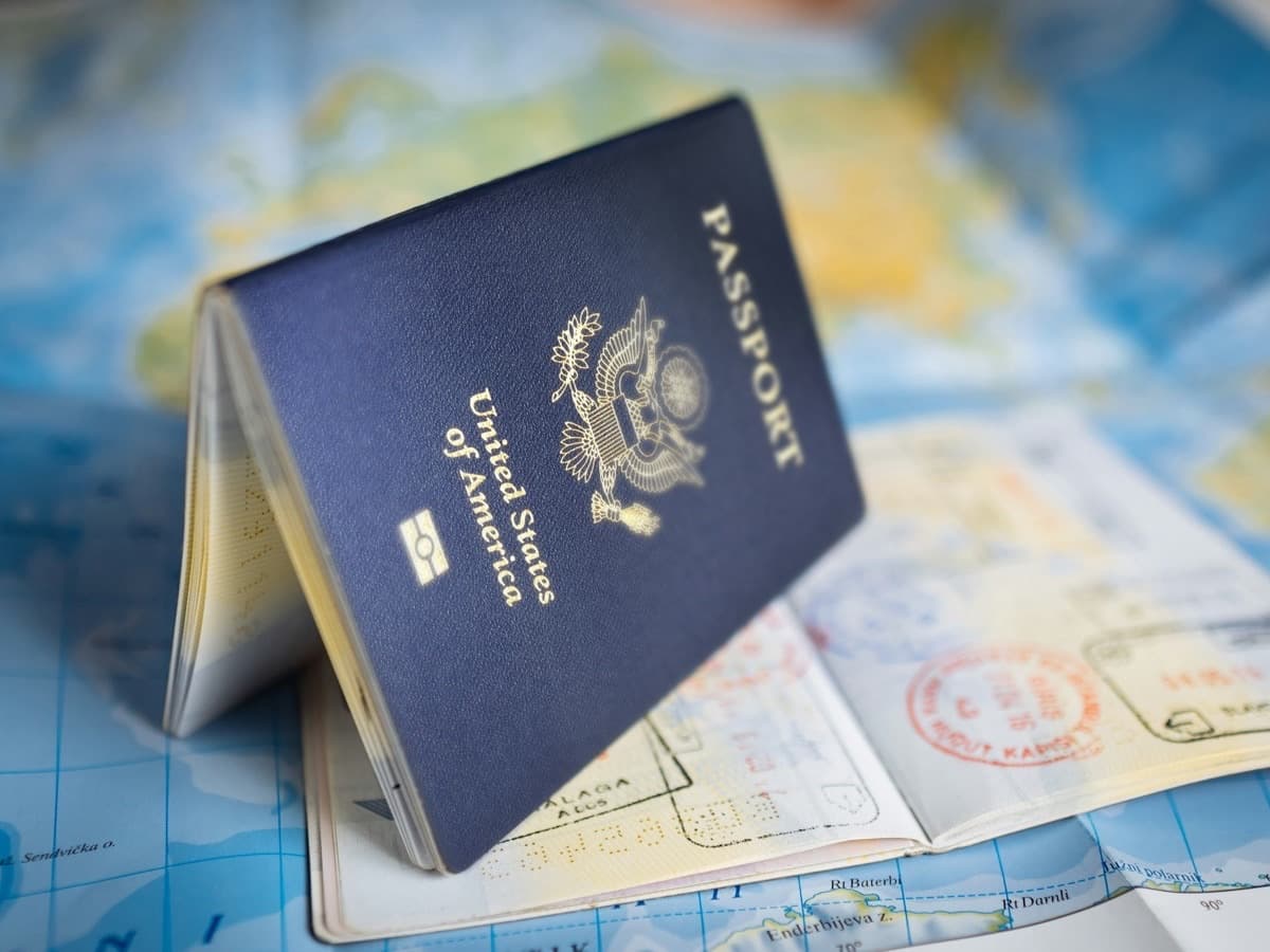 A United States passport standing open on a colourful world map, with a stamped passport page beneath it