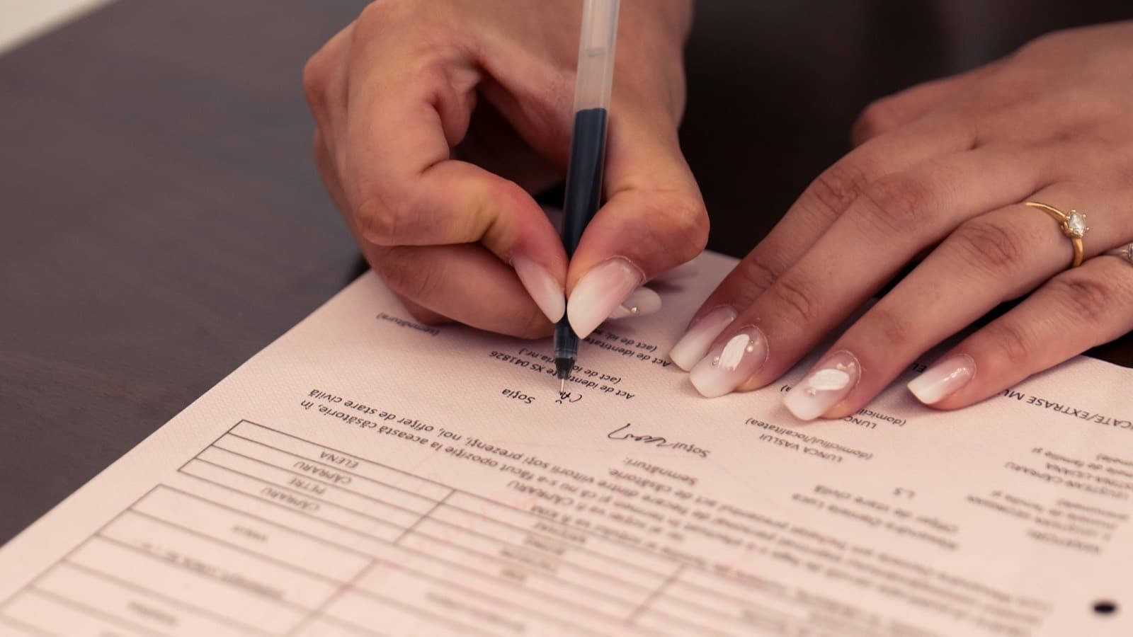 A person signing a printed document with a black pen on a dark table