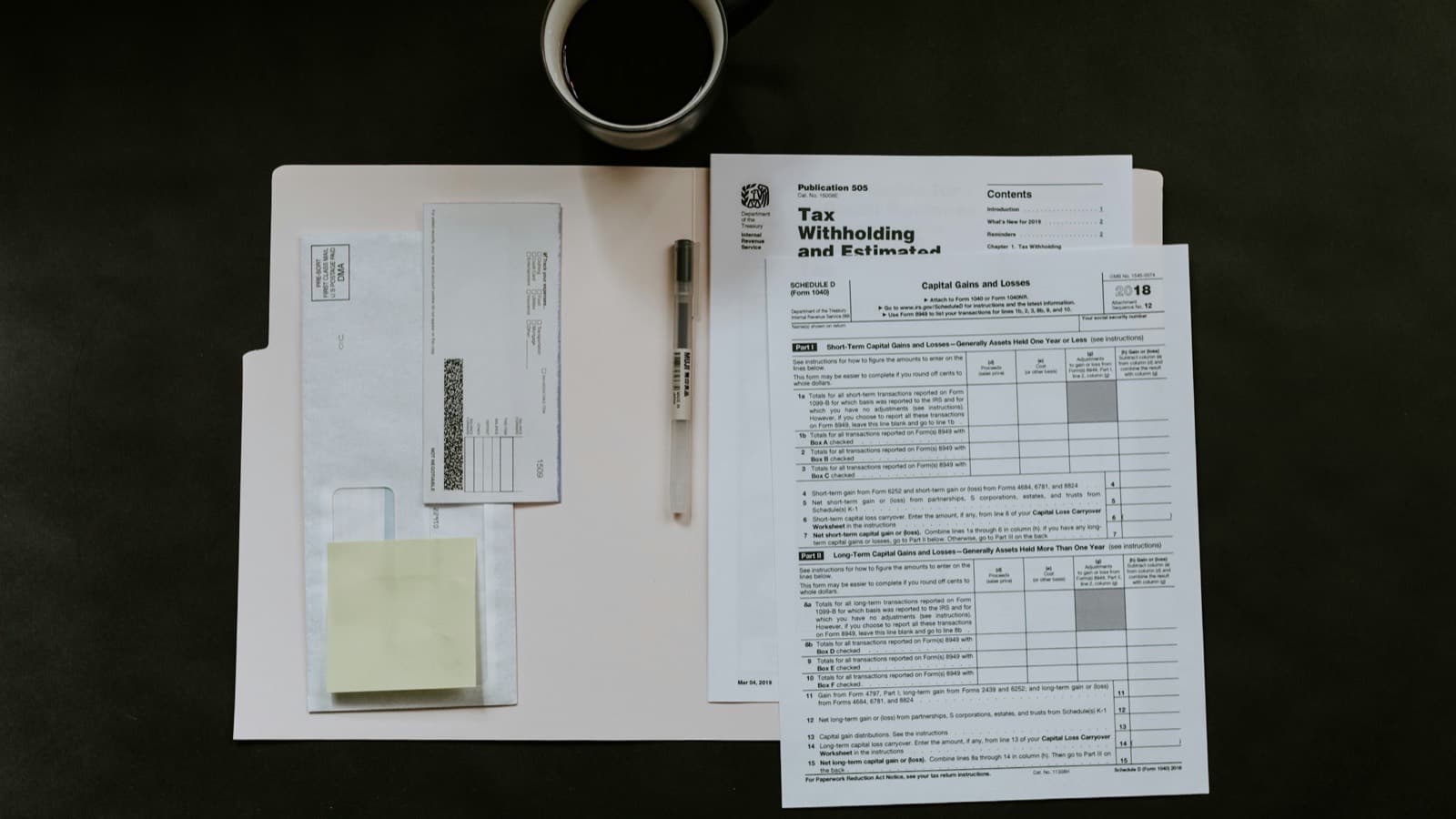 Tax return forms, a pen and a cup of coffee laid out on a dark desk