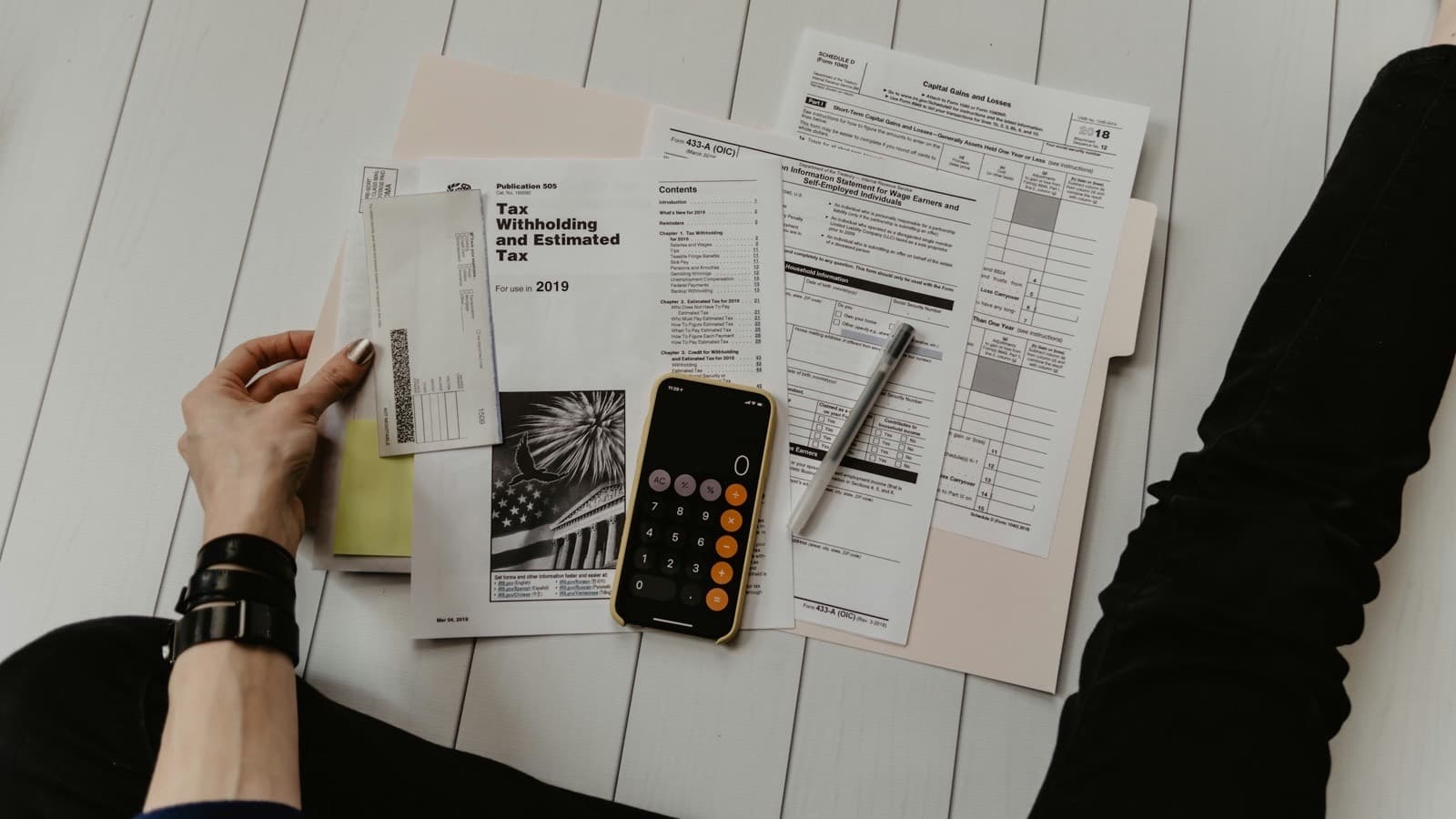 A person holding a sheet of paper beside a pen and a calculator