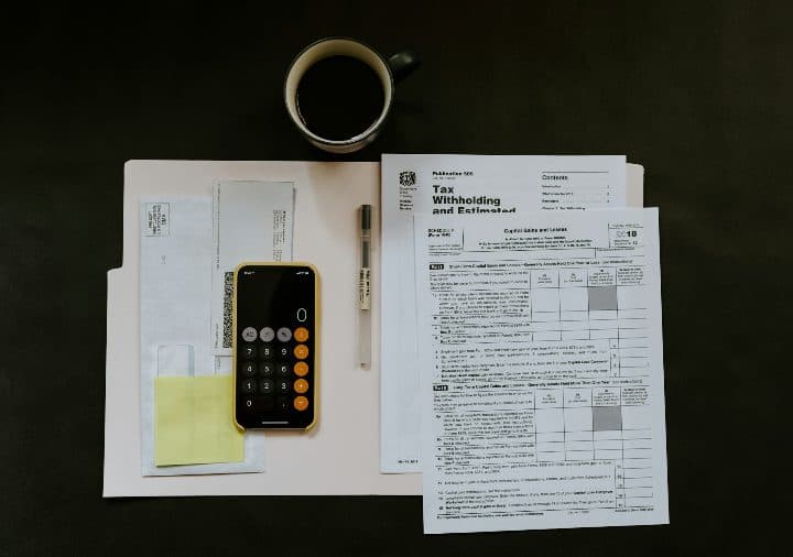 A smartphone and a ballpoint pen beside a tax certificate on a white folder