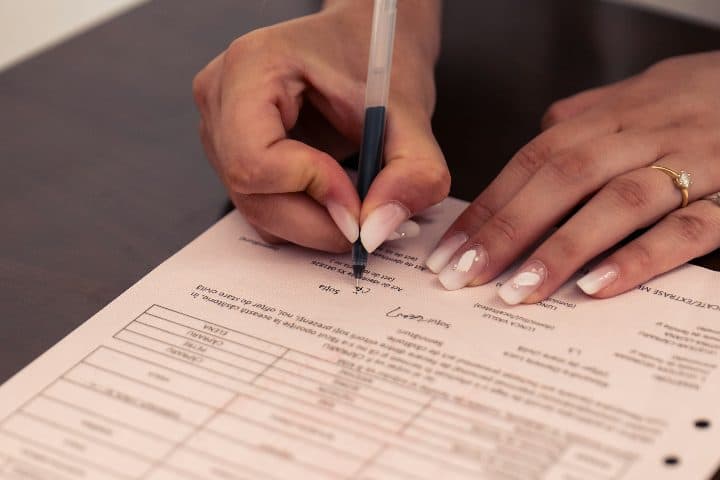 A person signing a printed document with a black pen on a dark table