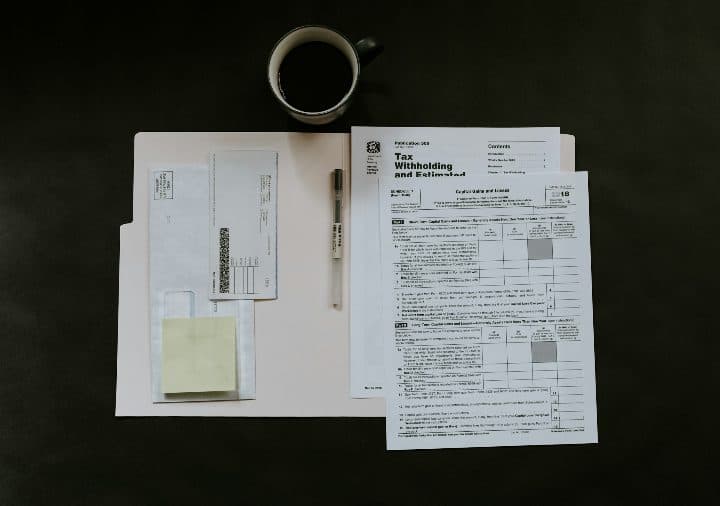 Tax return forms, a pen and a cup of coffee laid out on a dark desk