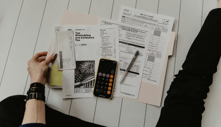 A person holding a sheet of paper beside a pen and a calculator