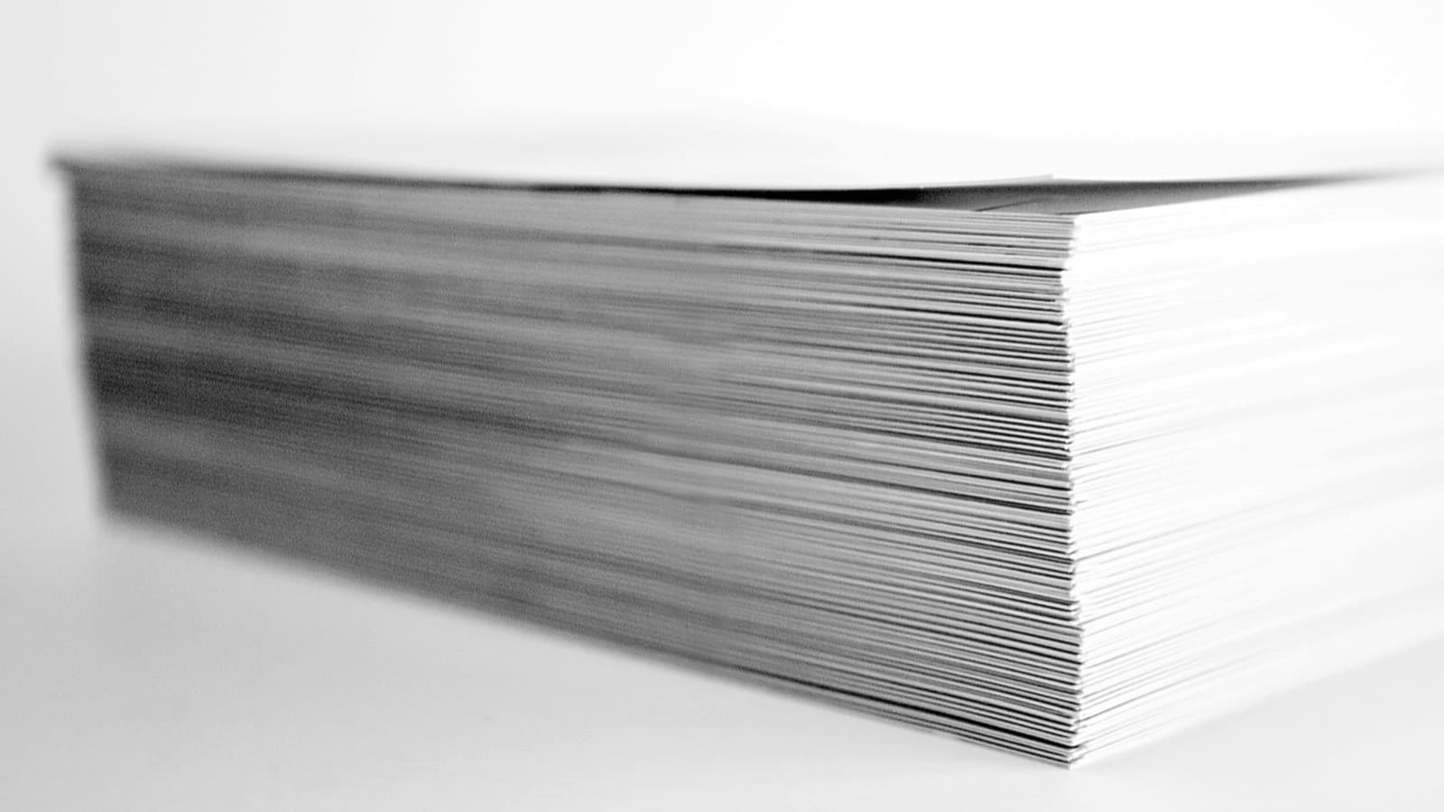 A black-and-white close-up of the edge of a thick stack of printed paper sheets on a plain white surface