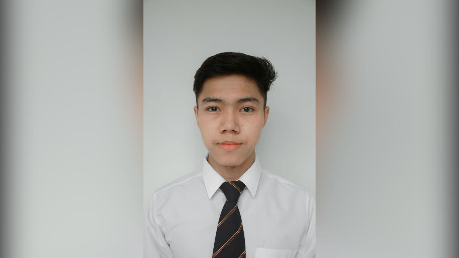 A young man in a white shirt and striped tie photographed head and shoulders against a plain white background